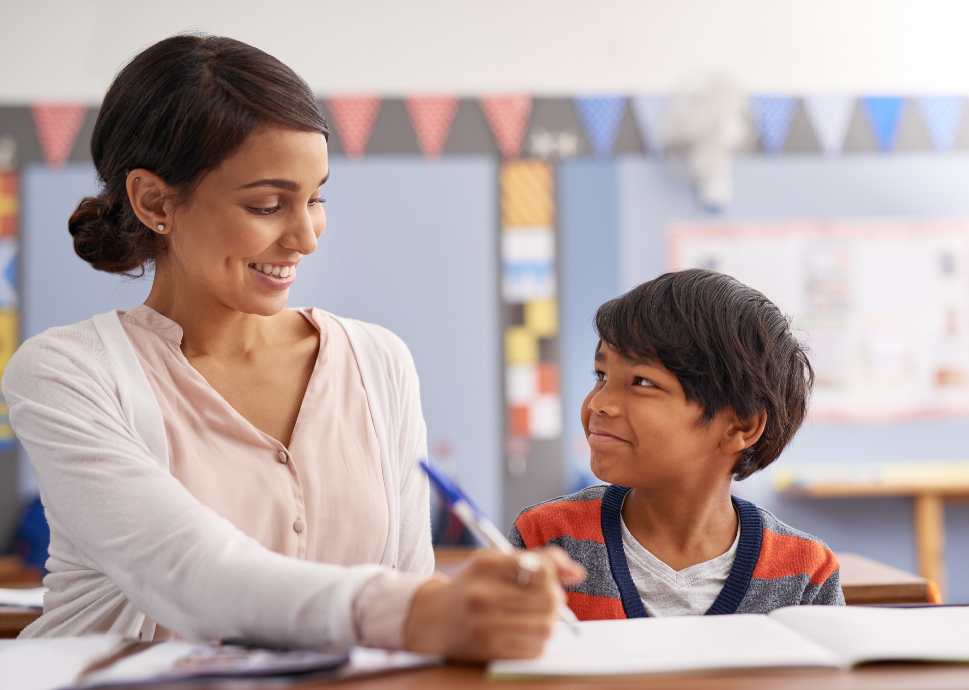 A teacher leaning in to guide a young student through their work